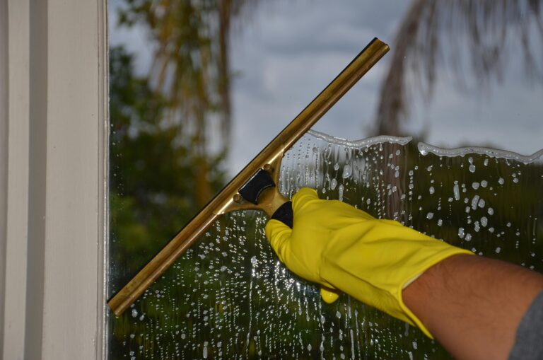Window Cleaning Close-up of hand cleaning window with squeegee outdoors using yellow gloves.